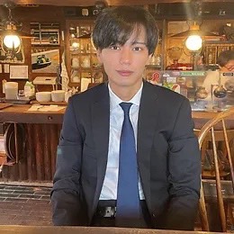 カフェらしき場所。黒のスーツに青いネクタイを付けて座っている男性。