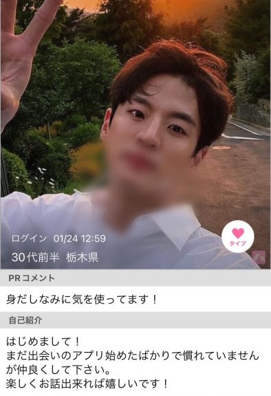 公園の道路らしき場所でピースをしながら自撮りをしている男性。白いシャツを着ている。