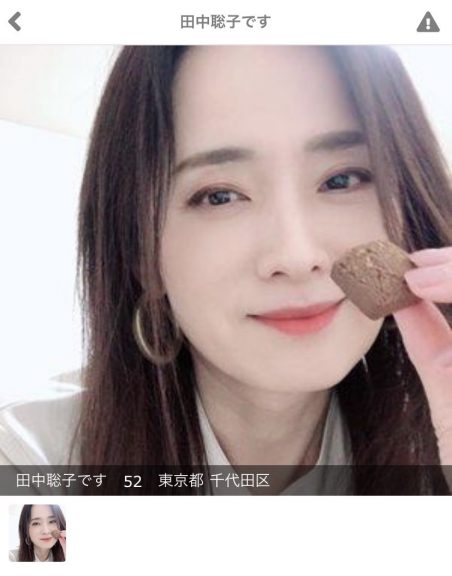 黒髪ロングヘアの女性が室内でクッキーを片手にこちらを見て微笑んでいる。