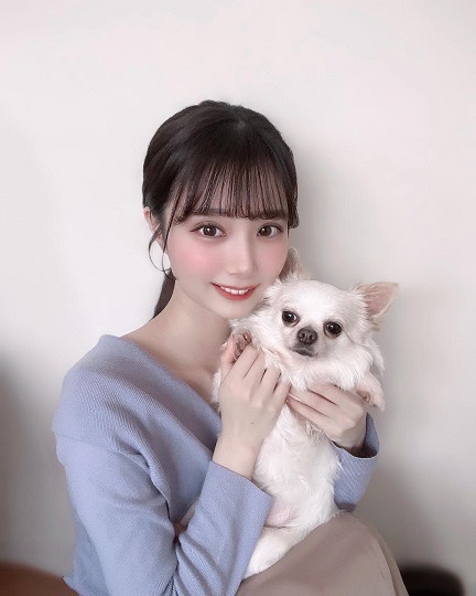 室内で白い犬を抱えてこちらに微笑む女性。犬はチワワ。女性は薄い青色のニットを着ていて、黒髪ロングヘア。髪は後ろで結っている。